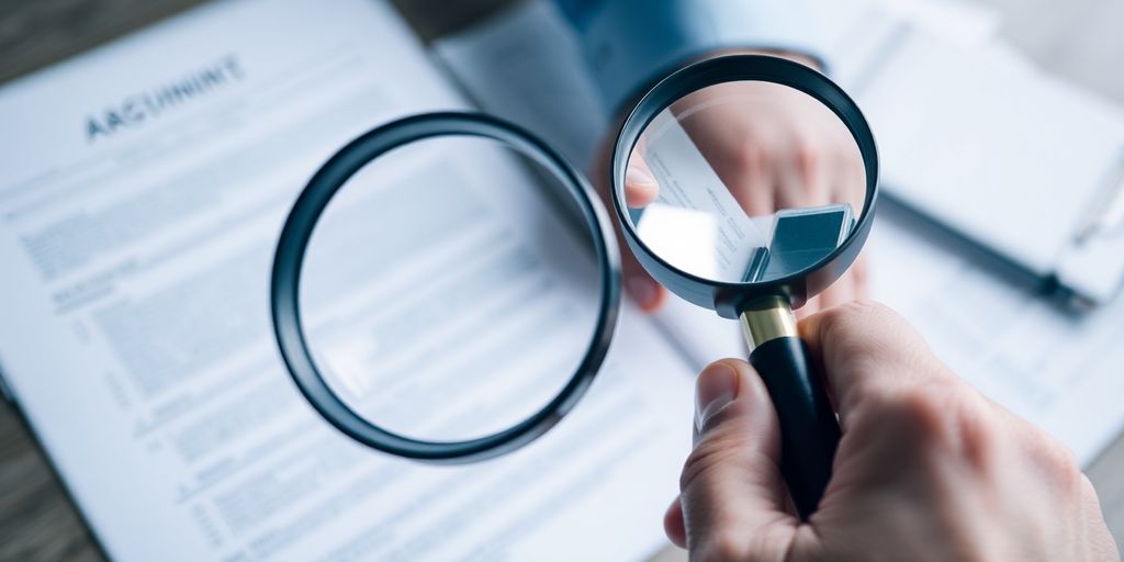 Person holding up a magnifying glass over legal documents.